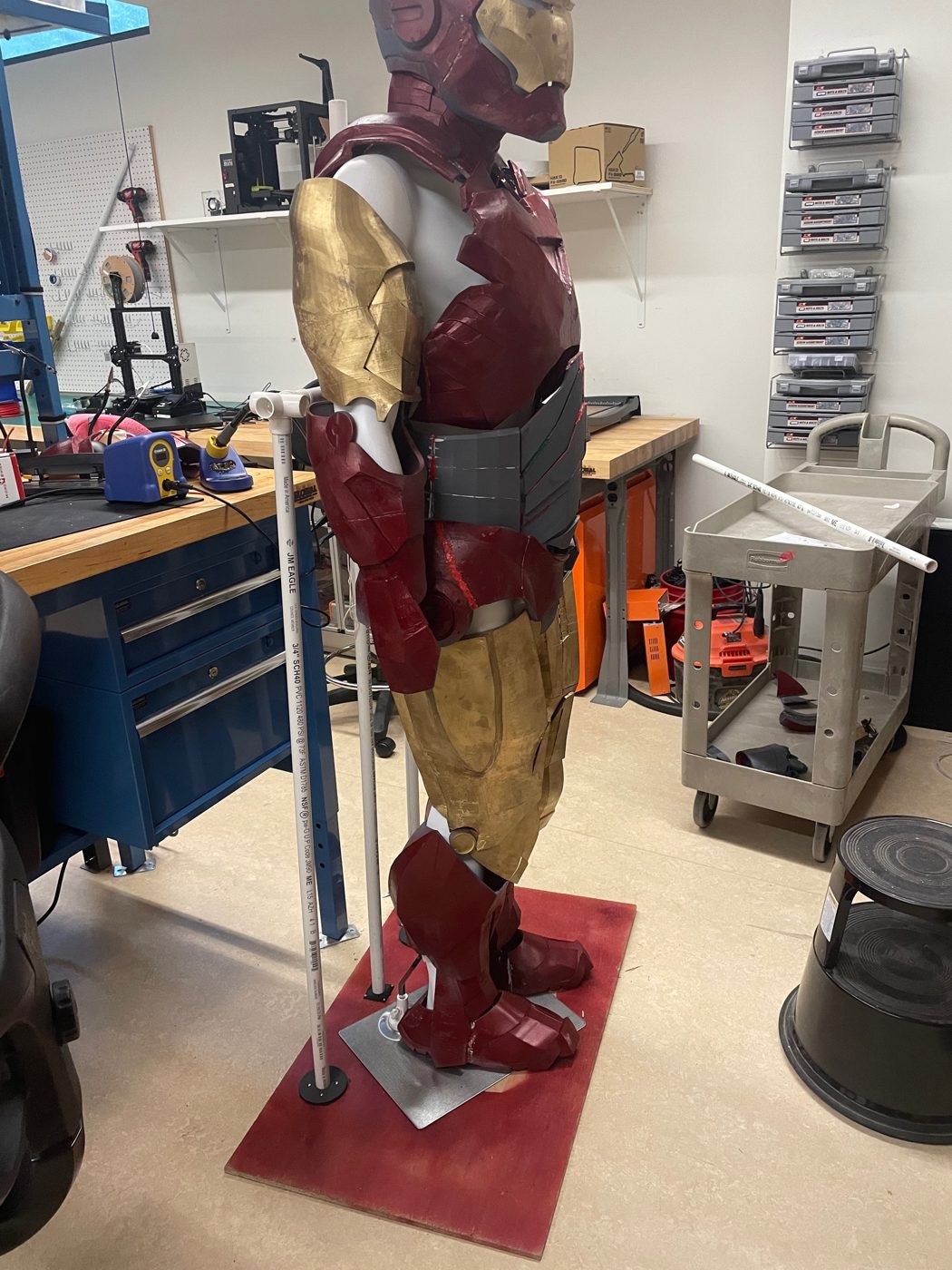 Side view of the full suit from our first attempt at propping it up, on a red plywood base with PVC pipe supports