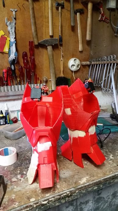 Printed red leg armor pieces on a workbench, held together with tape during assembly